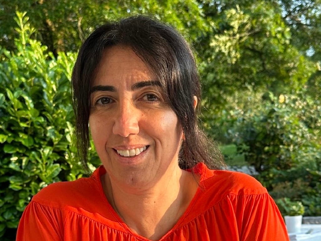 Porträt von Marta Alfia, Hospizleitung und Psychoonkologin (WPO), lächelnd in roter Bluse im Freien vor grünem Gartenhintergrund.