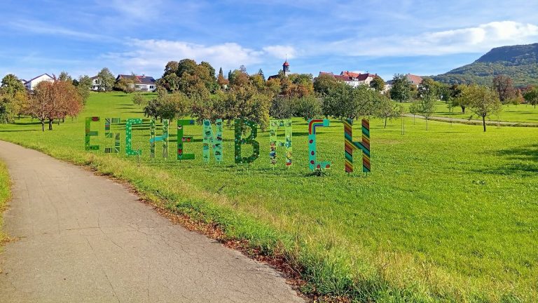 Bunte Eschenbach-Buchstaben auf einer grünen Wiese mit Blick auf den Ort und die Alb.
