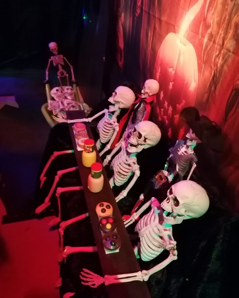 Halloween-Dekoration im Gruselgarten Bad Boll mit Skeletten an einem Tisch, bunten Getränken und Kerzenlicht in schauriger Atmosphäre