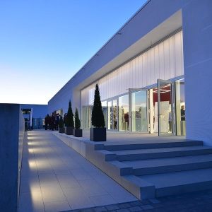 Eingangsbereich der Kulturhalle Süßen in der Abenddämmerung, modern beleuchtet mit Glasfassade und Besuchern im Hintergrund.