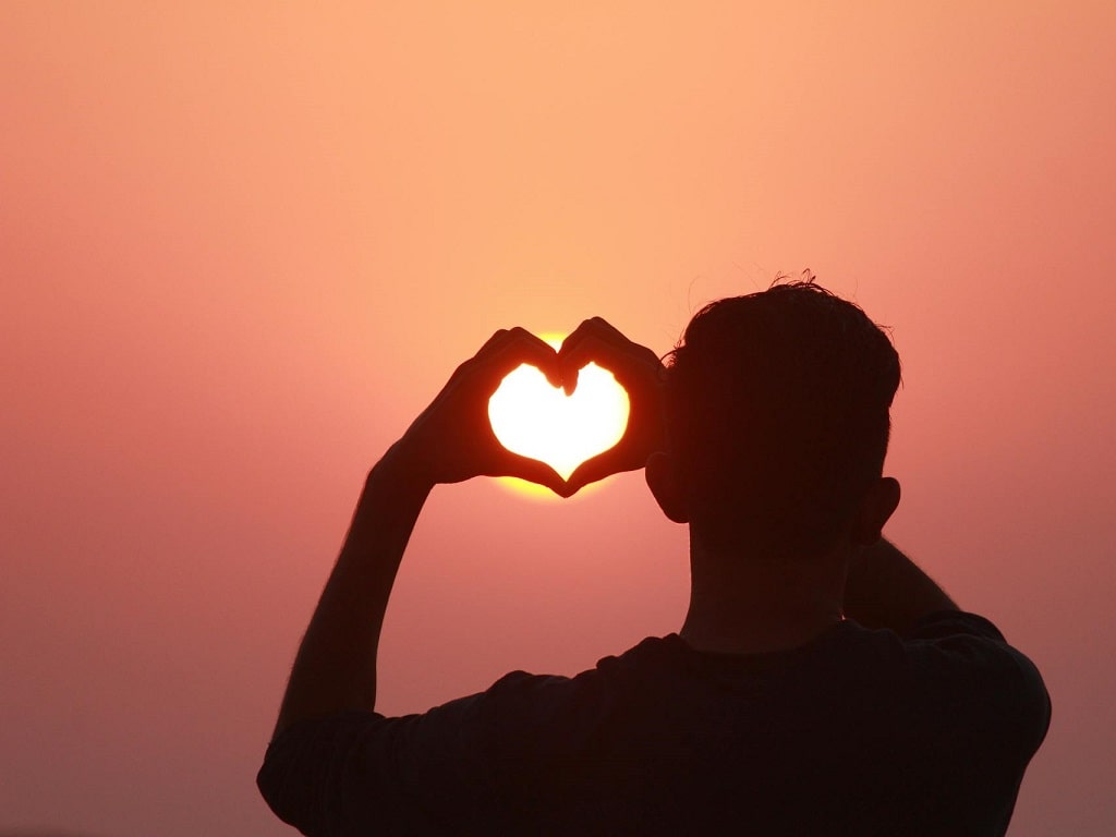 Person formt mit den Händen ein Herz vor der aufgehenden Sonne – Sinnbild für Gemeinschaft und Engagement während der WirWunderWoche zur Weltsparwoche 2025.