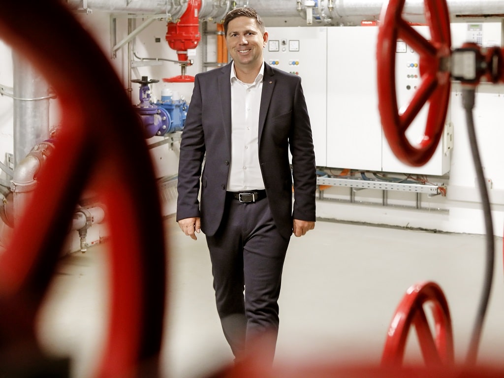 Alexander Lange, Geschäftsführer von FGM Gebäudemanagement, steht in einem Technikraum mit Rohrleitungen und großen roten Ventilrädern.