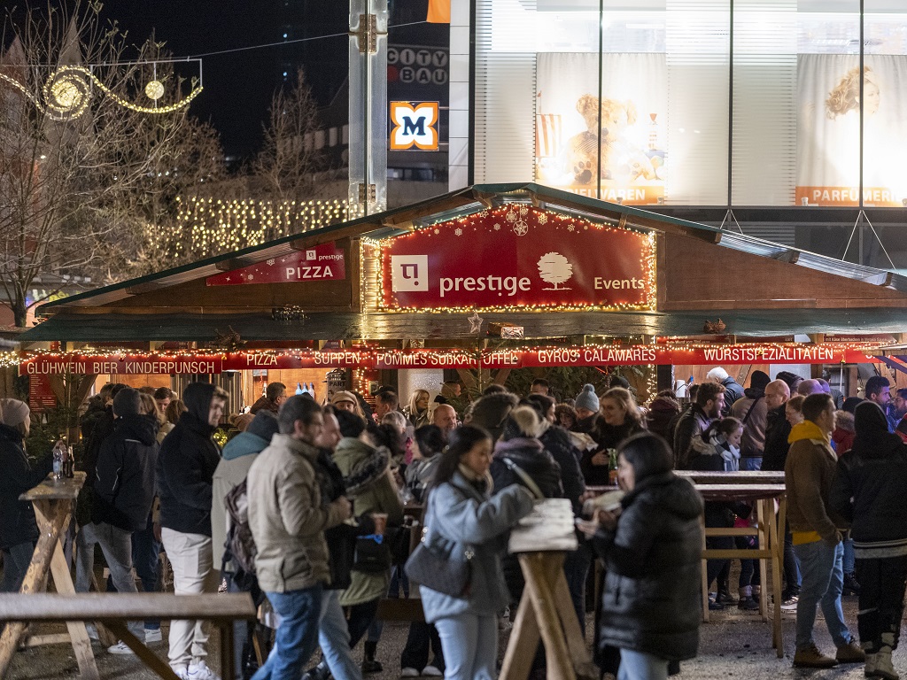 Abendstimmung auf der Waldweihnacht Göppingen: Besucher genießen Glühwein und Snacks an der festlich beleuchteten Hütte von Prestige Events auf dem Weihnachtsmarkt.
