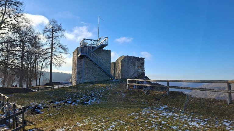 Burgruine Hiltenburg oberhalb von Bad Ditzenbach mit steinernen Mauern, moderner Metalltreppe zur Aussichtsplattform und Blick über die winterliche Hügellandschaft bei blauem Himmel.