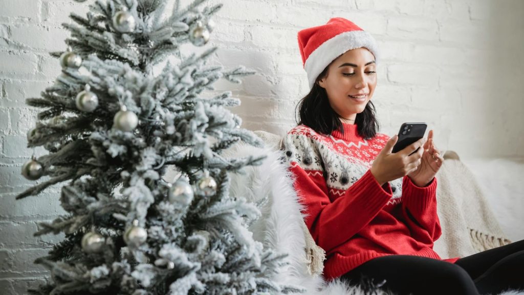 Person nutzt die App Sparkasse auf dem Smartphone in weihnachtlicher Atmosphäre neben einem Weihnachtsbaum.