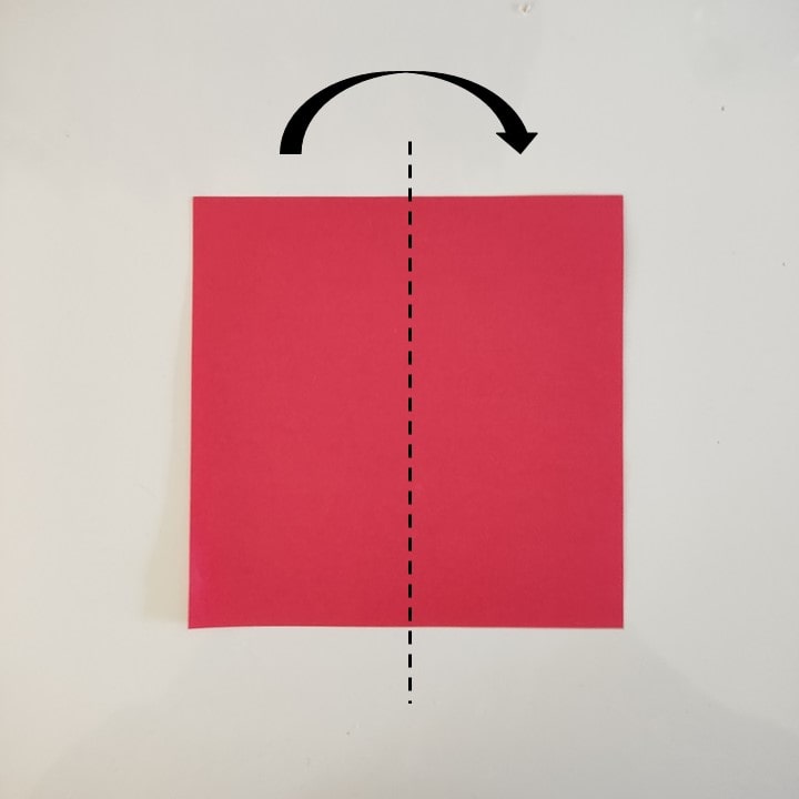 Quadratisches rotes Papier wird beim Schneeflocken-Scherenschnitt mittig von oben nach unten gefaltet, die Faltlinie ist gestrichelt markiert.
