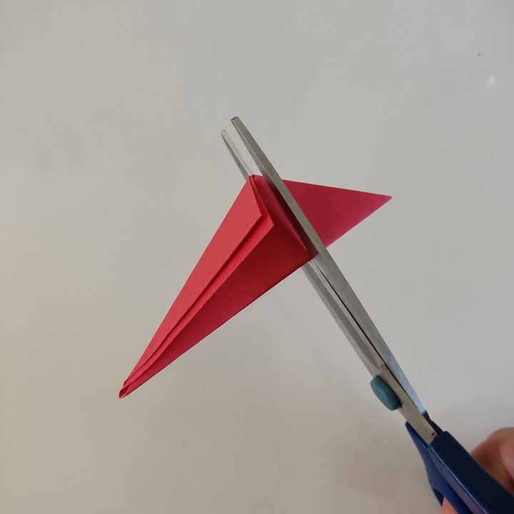 Die Spitze des mehrfach gefalteten Papiers wird mit einer Schere abgeschnitten.