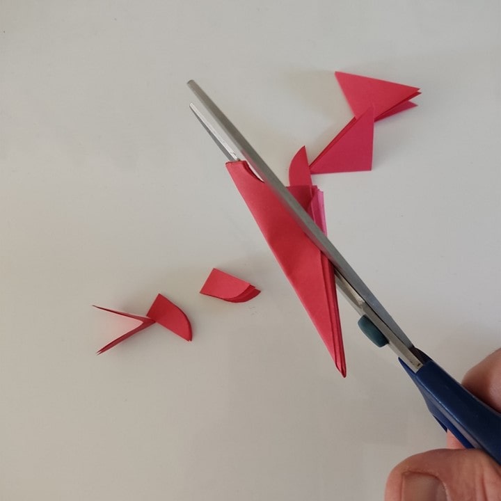 Beim Schneeflocken-Scherenschnitt werden mit der Schere verschiedene Formen aus dem gefalteten Papier ausgeschnitten.