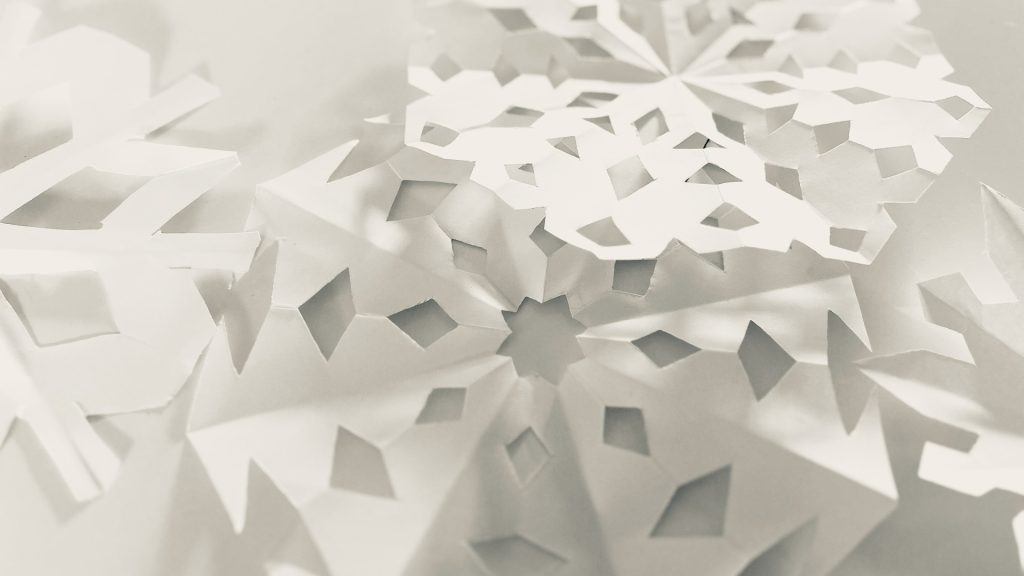Nahaufnahme von mehreren weißen Schneeflocken aus Papier mit unterschiedlichen ausgeschnittenen Mustern.