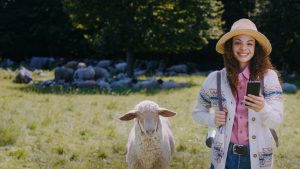 Frau mit Smartphone steht auf einer Wiese neben einem Schaf und symbolisiert digitalen Finanzüberblick mit Multibanking