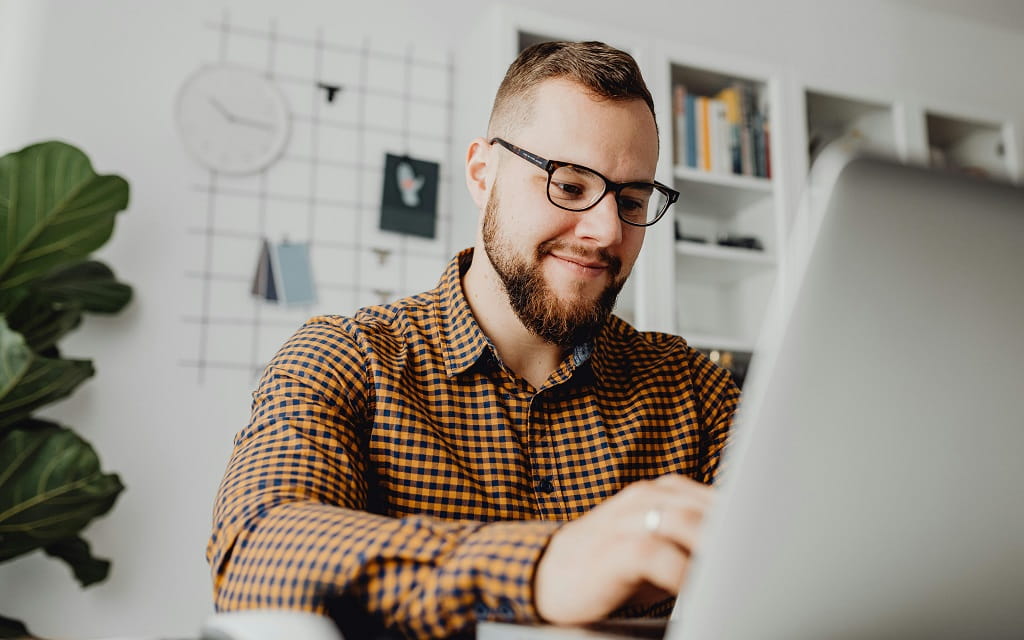Mann mit Brille arbeitet in einem hellen Homeoffice an einem Laptop um Bescheinigungen online anfordern zu können.