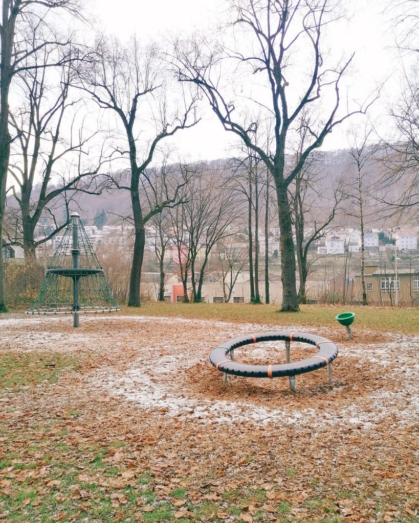 Spielbereich im Stadtpark Geislingen mit Drehscheibe und Kletterelementen, im Hintergrund Bäume und Blick auf die Stadt.