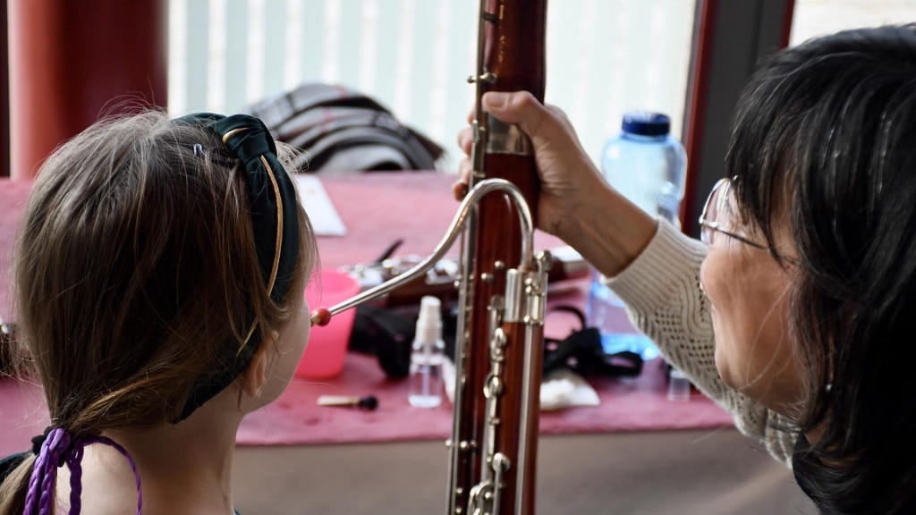 Lehrerin zeigt einem Kind im Unterrichtsraum ein Fagott und erklärt das Instrument.