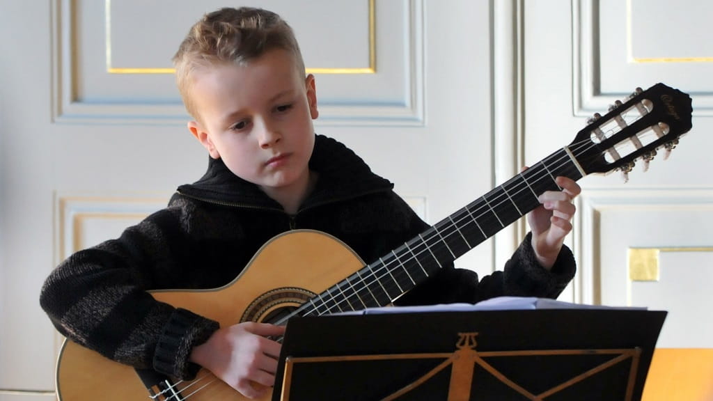 Ein Junge spielt konzentriert Gitarre bei der Instrumenteninformation der Jugendmusikschule Göppingen und liest dabei Noten vom Notenständer.