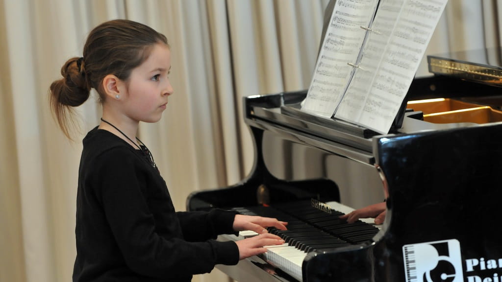 Ein Mädchen spielt konzentriert Klavier im Unterrichtsraum der Jugendmusikschule, vor ihr liegt aufgeklappte Noten.