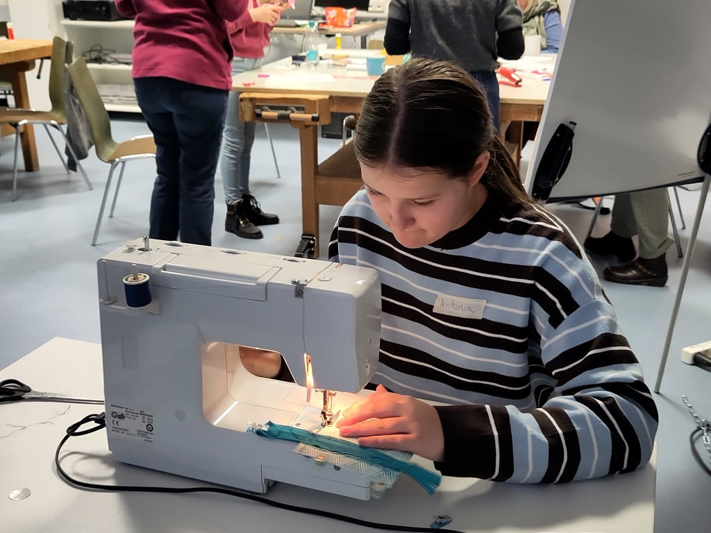 Teilnehmerin näht bei einem Upcycling-Workshop einen Geldbeutel aus recycelten Materialien an einer Nähmaschine.