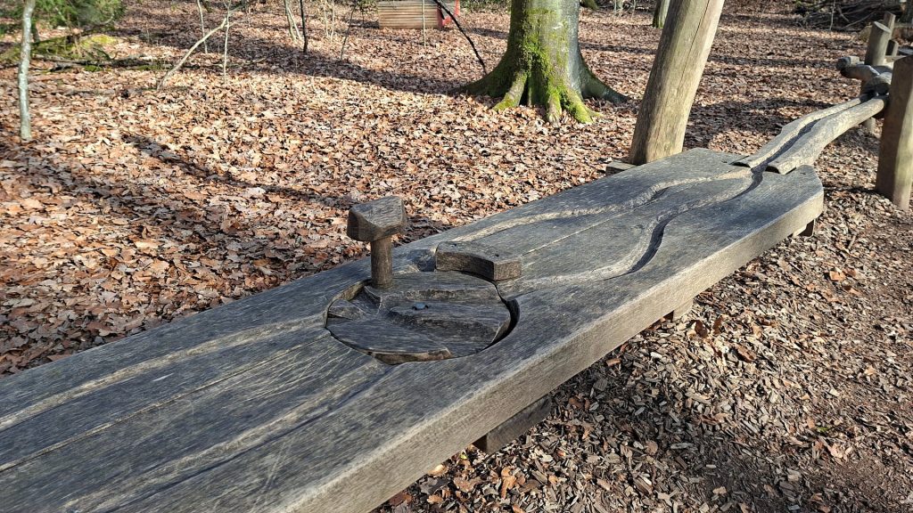 Waldmurmelbahn im Oberholz Göppingen mit geschnitzter Holzbahn und Startmechanismus inmitten eines Laubwaldes, natürliche Spielstation für Kinder entlang des Waldwegs