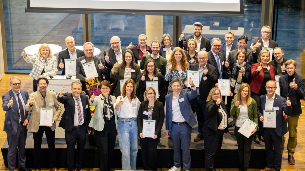 Gruppenfoto der ausgezeichneten Unternehmen bei der familyNET-Preisverleihung in Stuttgart für das Prädikat „Familienbewusstes Unternehmen“. Die Teilnehmenden halten ihre Urkunden und zeigen mit erhobenem Daumen ihre Auszeichnung.