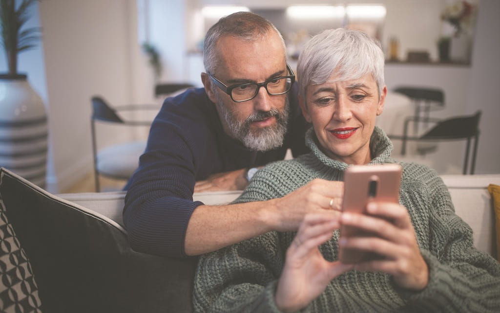 Paar sitzt gemeinsam auf dem Sofa und nutzt ein Smartphone für Online-Banking und digitale Services im Alltag und gewinnt dabei mehr digitales Vertrauen