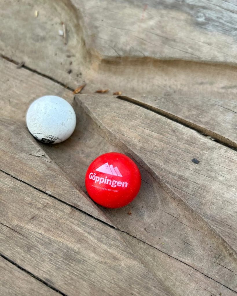 Zwei Murmeln liegen auf einer Holz-Kugelbahn, eine rote mit Aufdruck Göppingen und eine helle daneben.
