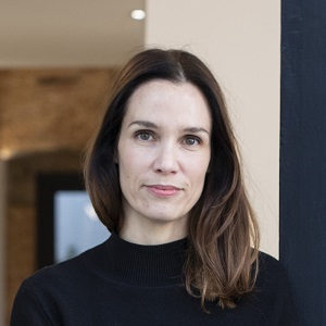 Porträt von Carolin Kreutzer vor neutralem Hintergrund, die ruhig in die Kamera blickt.