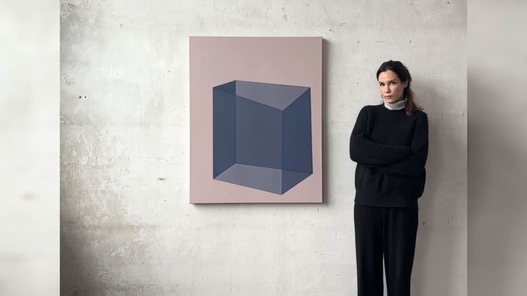 Künstlerin Carolin Kreutzer steht neben einem großformatigen, geometrisch-abstrakten Gemälde in gedeckten Farben vor einer schlichten Atelierwand.