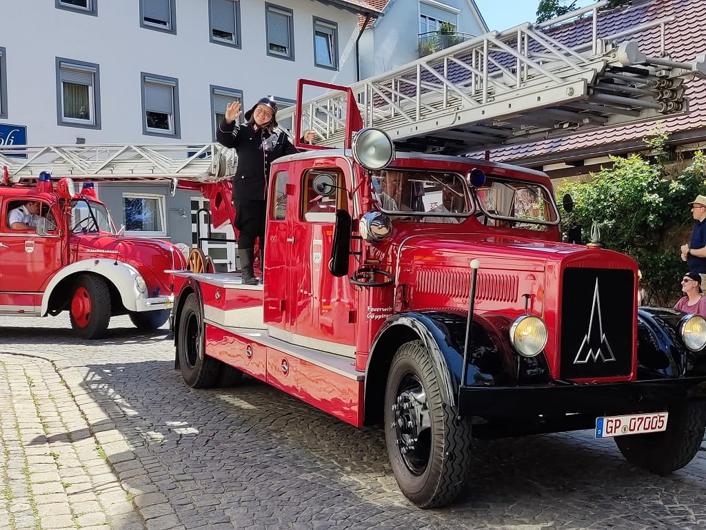 Ein rotes historisches Feuerwehrfahrzeug fährt beim Göppinger Maientag durch die Innenstadt, begleitet von Zuschauerinnen und Zuschauern am Straßenrand.
