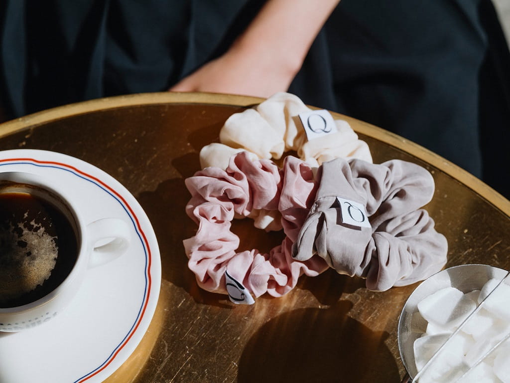 QUPRO-Scrunchies aus veganer Seide liegen auf einem Cafétisch neben einer Tasse Kaffee und Zucker.