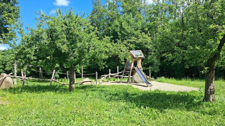 Spielplatz Katzenbach in Heiningen mit Rutsche, Holzelementen und Bäumen in naturnaher Umgebung.