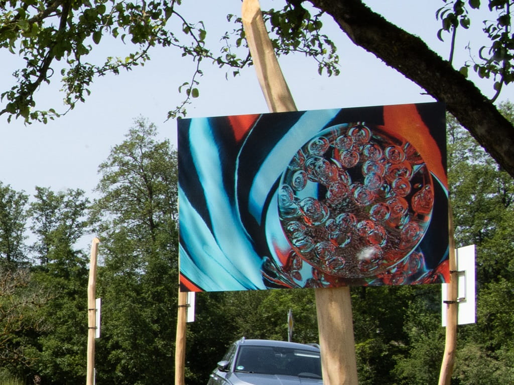 Eine farbige abstrakte Fotografie hängt auf einer Holzstele im Grünen und ist Teil der begehbaren Jubiläumsausstellung des Fotoclubs Albershausen.
