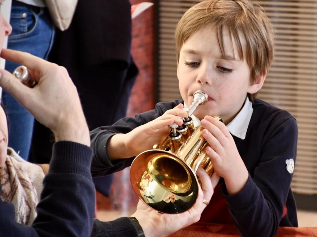 Ein Kind probiert bei der Städtischen Jugendmusikschule Göppingen eine Trompete aus und wird dabei von einer erwachsenen Person unterstützt.