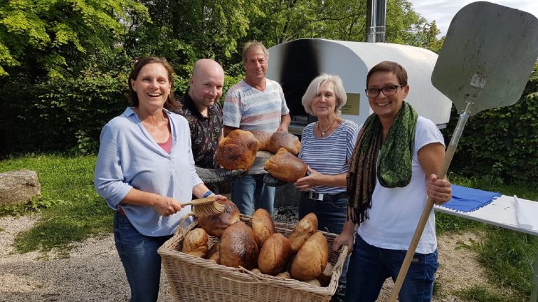Teilnehmerinnen und Teilnehmer beim Brotbacken auf dem Hohenstaufen präsentieren frisch gebackene Brote vor dem Holzbackofen.