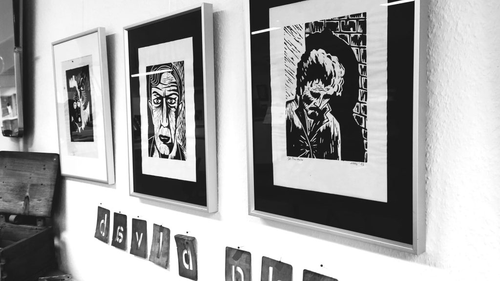 Schwarz-weißes Ausstellungsbild zu „Sucht & Kunst“ im MuSeele mit gerahmten Linoldrucken von J. K. Davidenko.