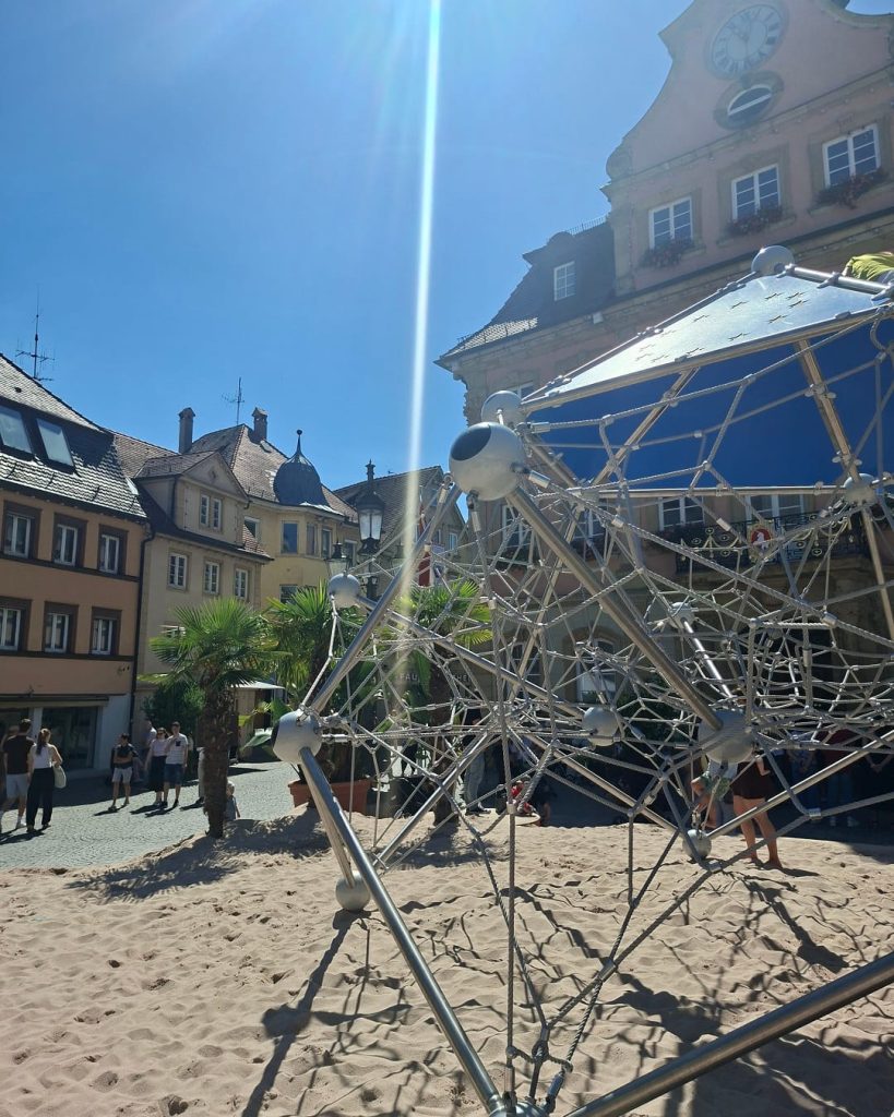 Großes Klettergerüst im Sand auf dem Pop-up-Spielplatz am Oberen Marktplatz in Schwäbisch Gmünd, umgeben von historischen Gebäuden.