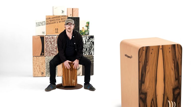 Martin „Mädde“ Sauer sitzt auf einer Cajon vor mehreren Cajons neben einer Schlagwerk-Cajon für den Cajon-Workshop auf dem Hohenstaufen.