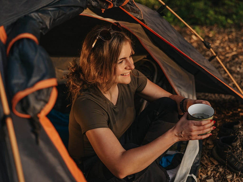 Eine Wanderin sitzt mit einer Tasse am Eingang ihres Zelts im Trekking-Camp bei Gingen an der Fils.