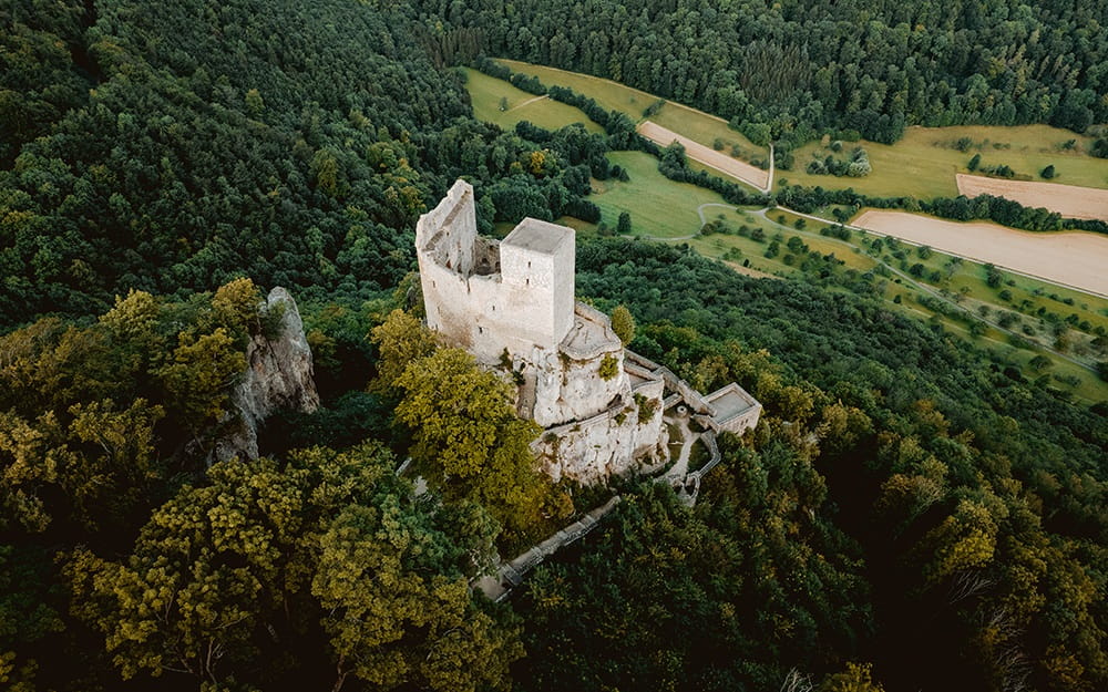 Luftaufnahme der Burgruine Reußenstein auf einem bewaldeten Felsen.