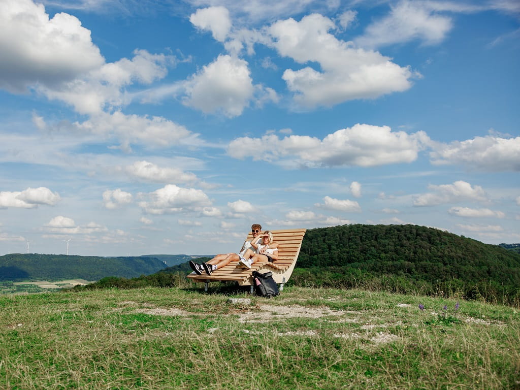 Paar auf einer Holzliege an einem Aussichtspunkt am Albtrauf mit weitem Blick über die Landschaft