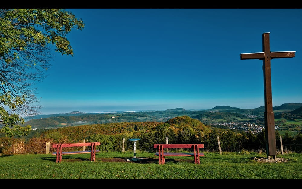 Aussicht von der Maierhalde mit Sitzbänken, großem Holzkreuz und weitem Blick über die Landschaft am Albtrauf.
