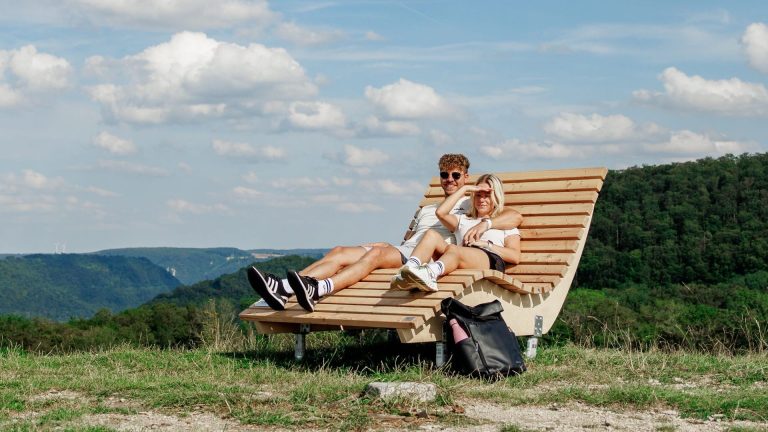 Paar auf einer Holzliege an einem Aussichtspunkt am Albtrauf mit Blick über die Landschaft