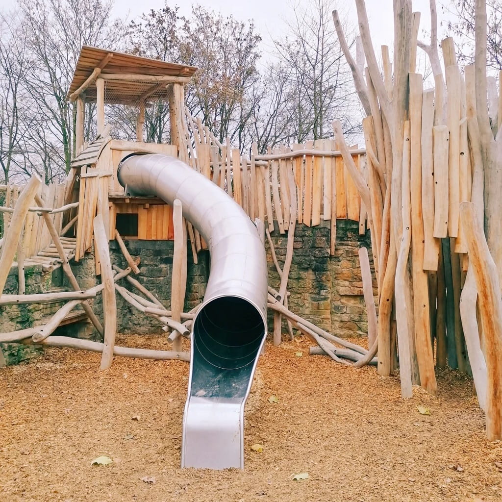 Spielplatz in Göppingen-Faurndau mit einem hölzernen Kletterturm, einer großen Röhrenrutsche aus Metall und einer naturnahen Kletteranlage aus Baumstämmen.