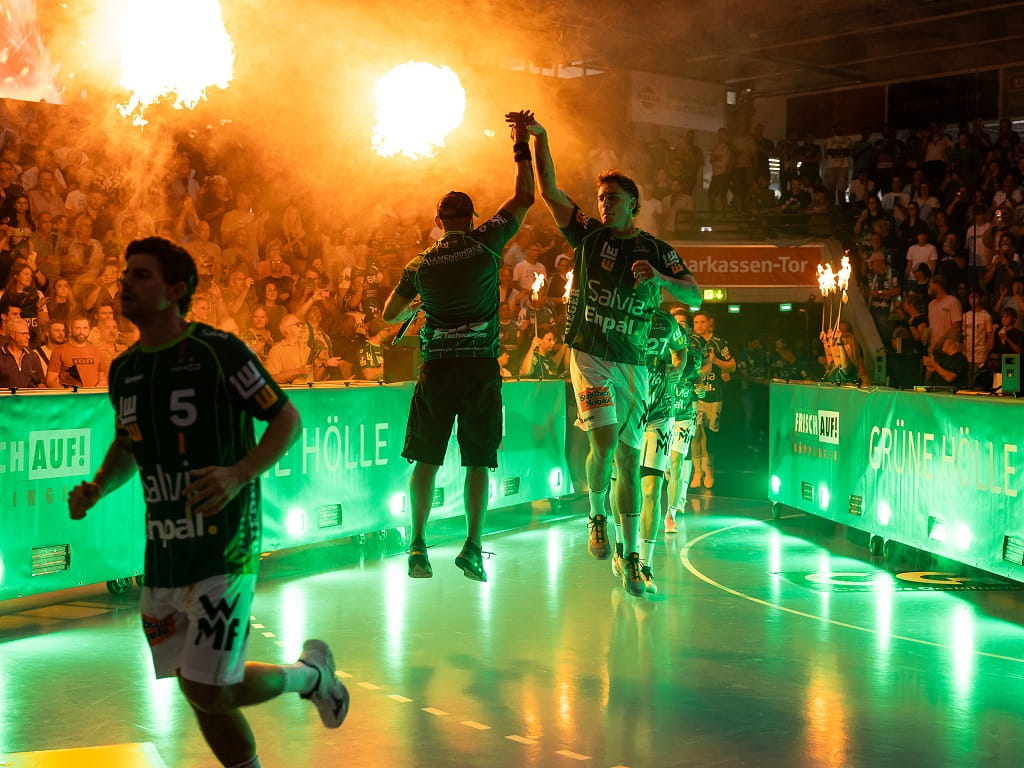 Spieler von FRISCH AUF! Göppingen laufen unter Feuerfontänen und grüner Beleuchtung in die EWS Arena ein.