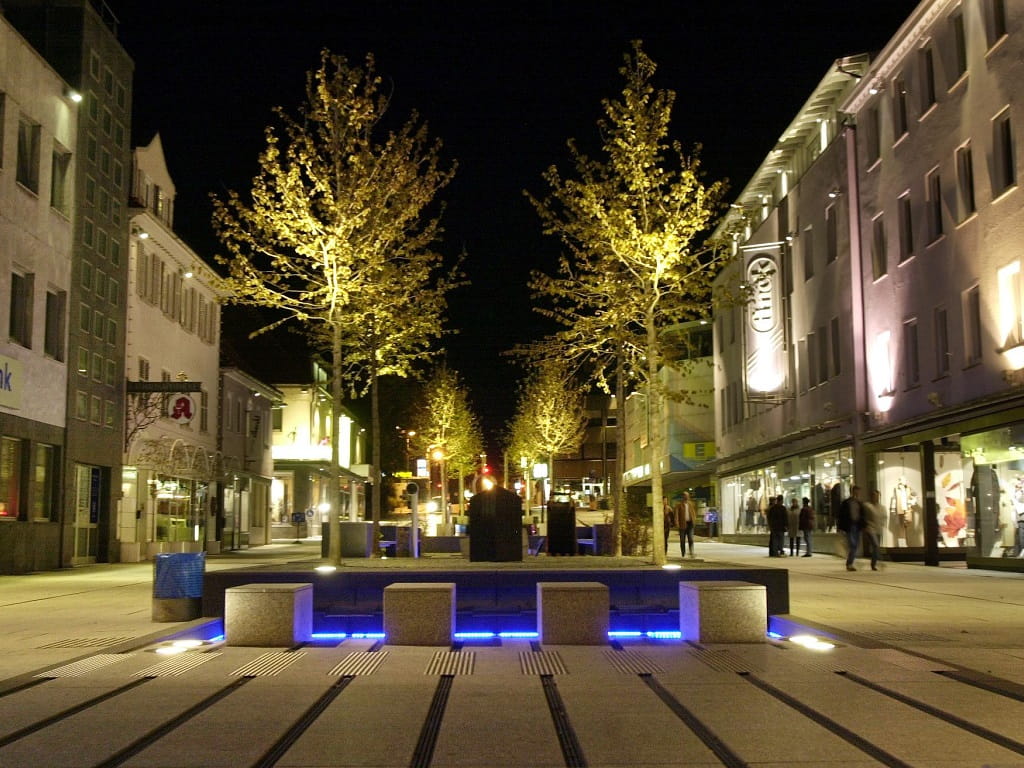 Beleuchtete Bäume, Gebäude und Wasserspiel in der Neuen Mitte in Göppingen bei Nacht.