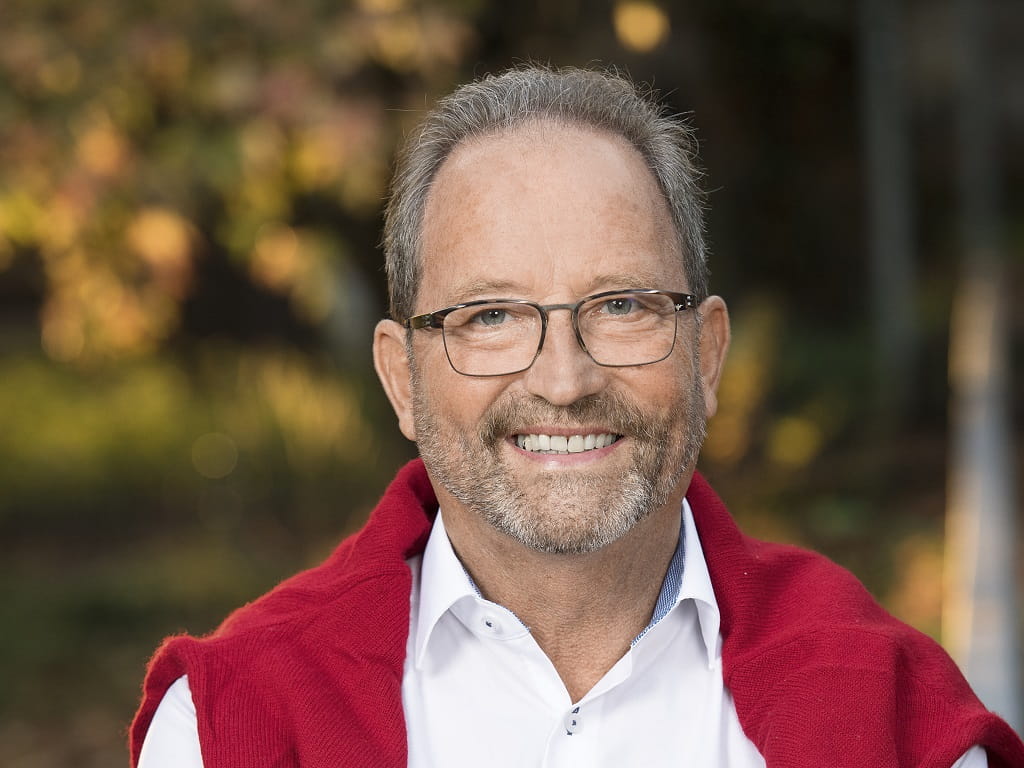 Porträt des Göppinger Stadtführers Rudi Bauer mit Brille, weißem Hemd und rotem Pullover vor unscharfem Hintergrund.