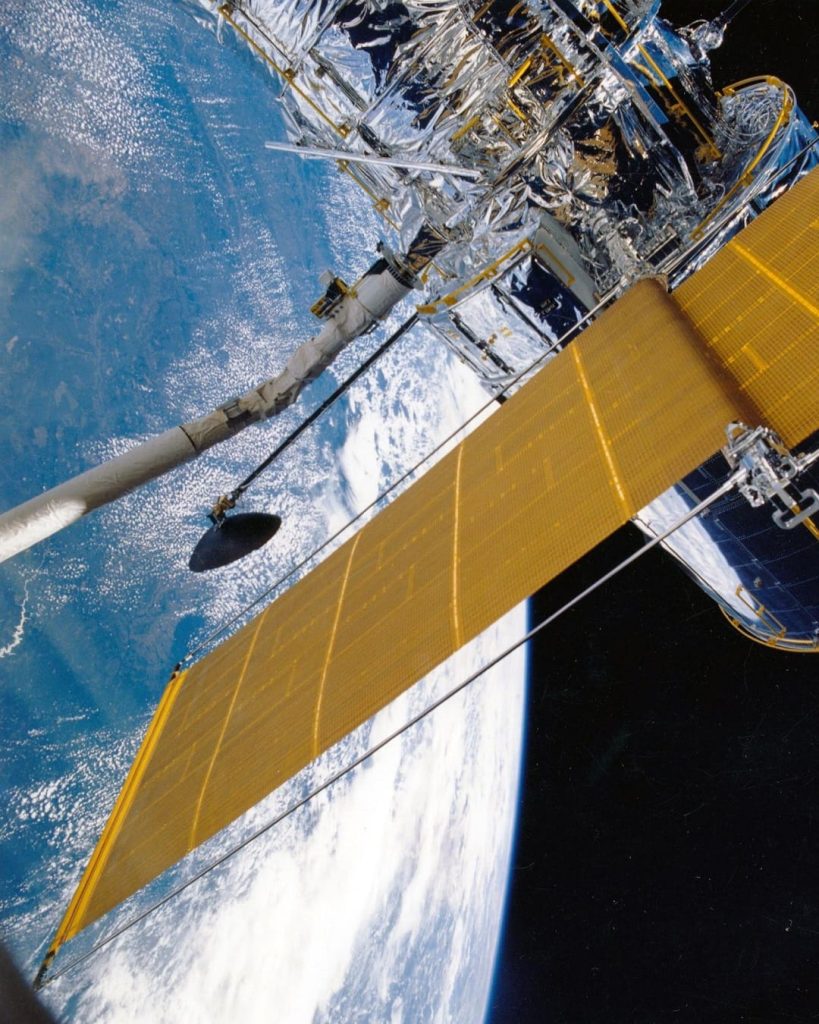 Weltraumteleskop mit goldenen Solarpaneelen über der Erde als Symbolbild für die Vortragsreihe Raumfahrt.